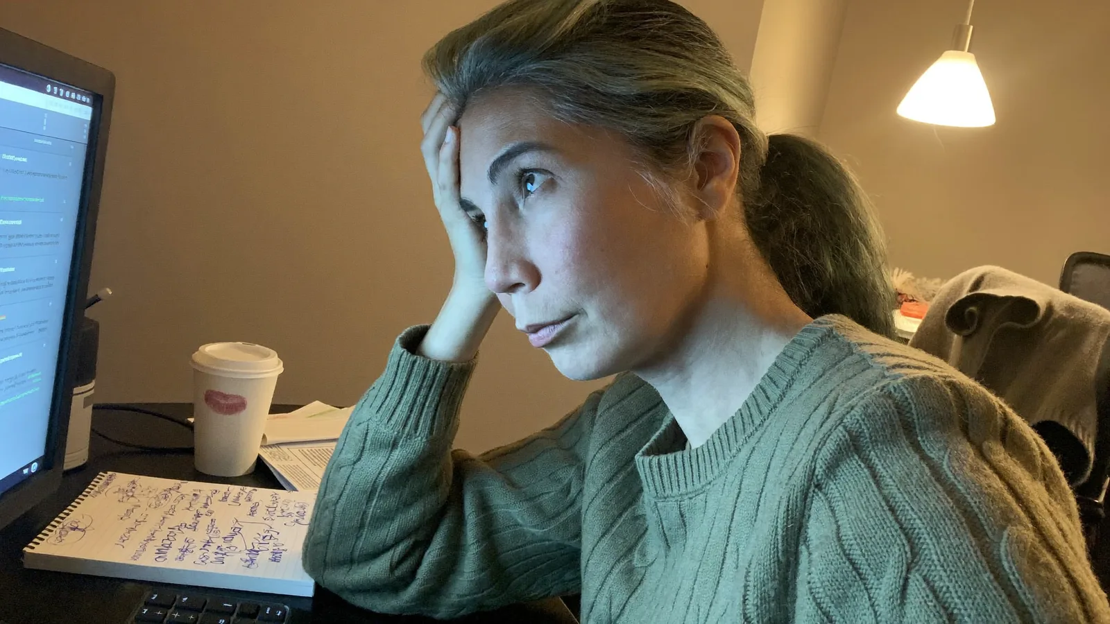 En kvinna vid sitt skrivbord med fingrarna tryckta mot tinningen